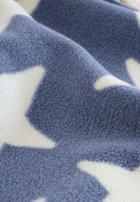 Fleece-tæppe med en mørkeblå overflade, store hvide stjernemønstre, blød tekstur og en let fnugget finish.