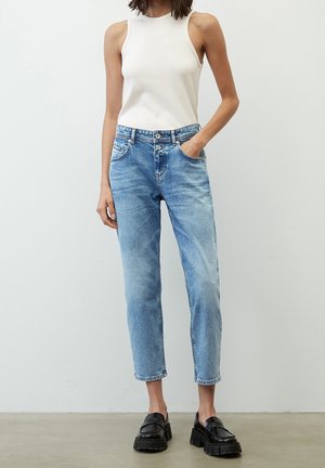 Jeans de tiro alto color azul claro con pierna ajustada, con un lavado desgastado, dos bolsillos frontales y cierre de botón. Mocasines negros gruesos.