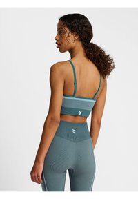 Sujetador deportivo en color verde azulado con textura acanalada, tirantes finos ajustables y un patrón de rayas blancas en contraste. Combinado con leggings de cintura alta a juego.