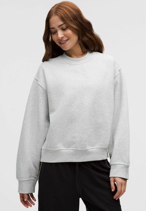 Hellgrauer Pullover mit rundem Ausschnitt, überschnittenen Schultern und gerippten Bündchen, kombiniert mit schwarzen Hosen. Weiches Baumwollmischmaterial.