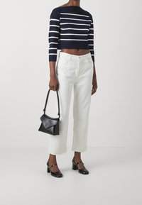 Pullover corto a righe navy e bianche, jeans bianchi a gamba larga, borsa nera strutturata e scarpe con tacco blocco nere e cinturini alla caviglia.