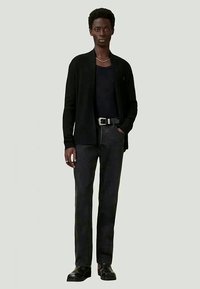 Sort cardigan over en mørk t-shirt, parret med sorte jeans og sorte støvler. Enkelt design, skræddersyet pasform, og glat tekstur.