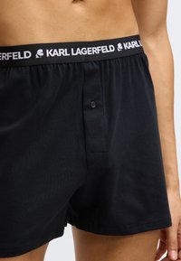 Μαύρα βαμβακερά μποξεράκια με λευκή ελαστική μέση και κουμπωτό καβαλέτο, με ραμμένες λεπτομέρειες και απαλό υφή.