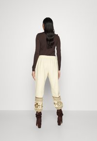 Krämfärgade joggerbyxor med ett mönstrat avslut i brunt och elfenben. Matchat med bruna, rynkiga ankelboots och en mörkbrun långärmad topp.