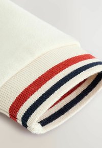 Crème trui manchet met een geribbelde rand in rood en marineblauw gestreept. Het materiaal heeft een zachte textuur met een gladde afwerking.