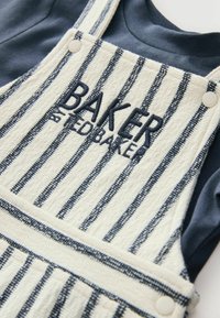 Ribatud beežid ja tumesinised puuvillased üleüldised, millel on reguleeritavad rihmad, esitatud broderi "BAKER by Ted Baker" ja nööbi aktsentidega.