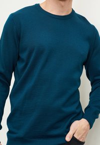 Miętowy sweter z okrągłym dekoltem, długimi rękawami, ściągaczami przy mankietach i dole, wykonany z miękkiej dzianiny o gładkiej fakturze i klasycznym kroju.