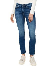 Niebieskie dżinsy skinny z detalami w postaci wyblakłych miejsc, pięcioma kieszeniami i paskiem, w połączeniu z białymi sneakersami z teksturowaną podeszwą.