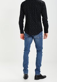 Maglietta nera a maniche lunghe con motivo blu, abbinata a jeans in denim blu e scarpe nere. Stile casual con design aderente.