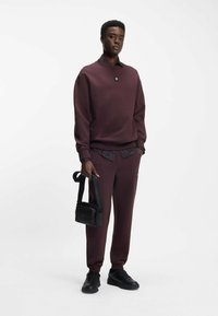 Maroon sweatshirt with round neckline, smooth texture, paired with matching pants. Black crossbody bag and sneakers complete the look.
