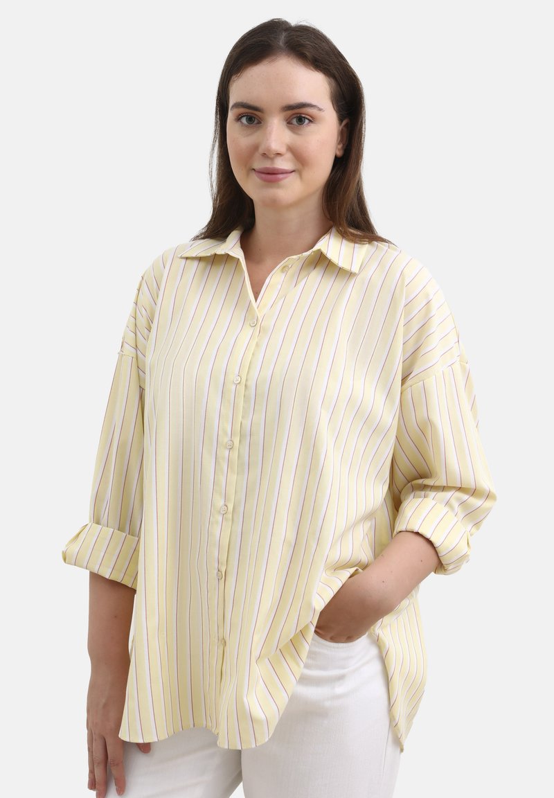 Camicia giallo chiaro con bottoni, caratterizzata da righe verticali viola, taglio rilassato, maniche lunghe arrotolate e colletto a punta.