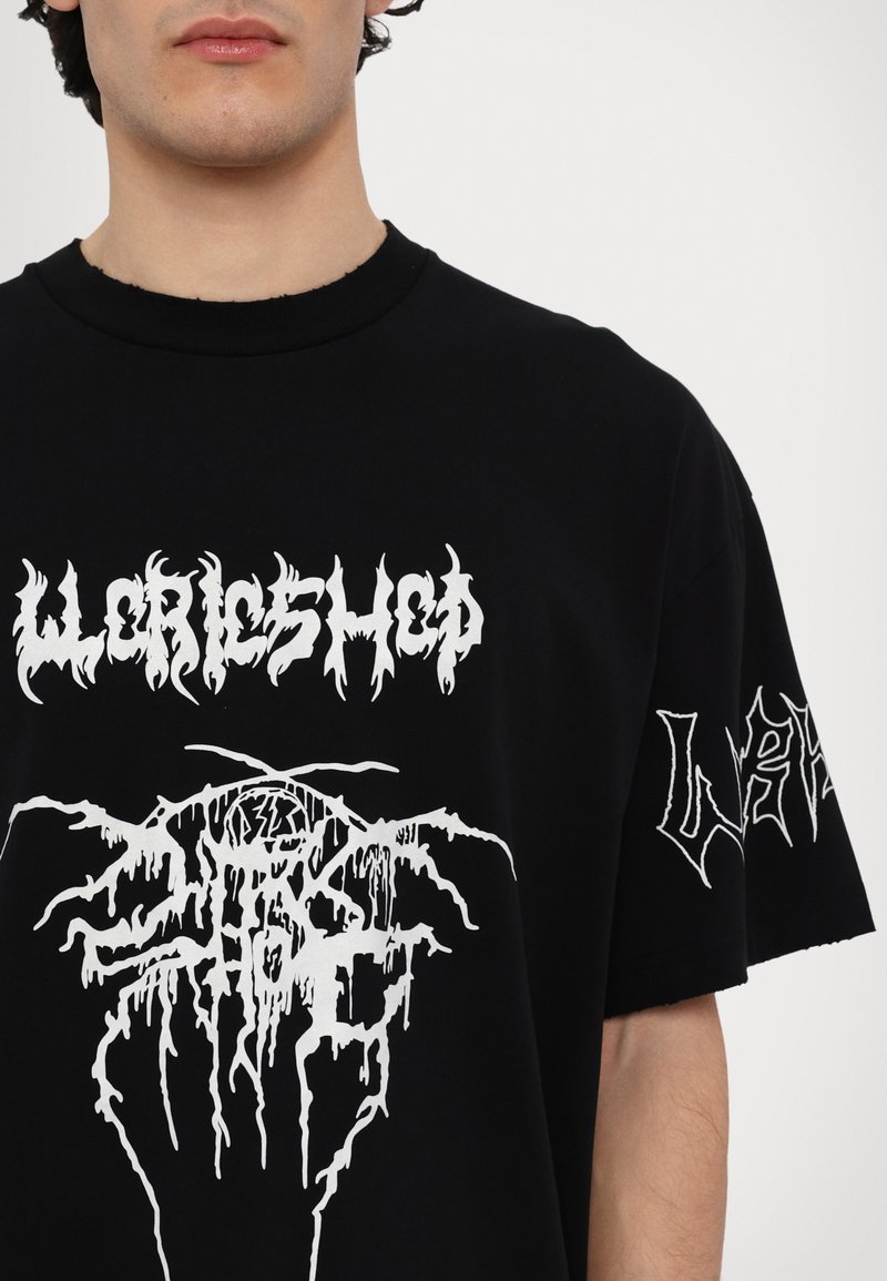 Sort bomulds T-shirt med store hvide grafiske tryk på forsiden og ærmet. Designet inkluderer stiliseret, abstrakt skrift og former.