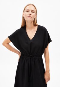 Schwarzes Leinenkleid mit V-Ausschnitt, kurzen Ärmeln und taillierter Taille mit Kordelzugdetails. Glatte Textur und minimalistisches Design.