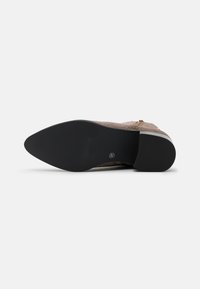 Suela de un zapato beige con una parte inferior de goma negra de textura, que muestra un diseño elegante y un detalle de cremallera en el lateral.