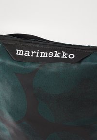 Borsa nera e teal con una finitura liscia e strutturata; presenta l'etichetta "marimekko" in bianco e una cerniera scoperta nella parte superiore.
