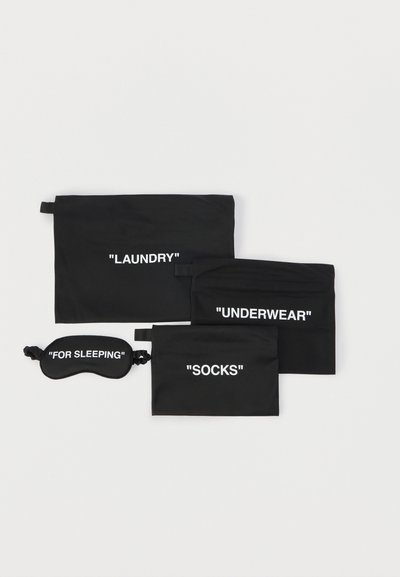Τέσσερις μαύροι ταξιδιωτικοί σάκοι και μία μάσκα ύπνου με τις επιγραφές «ΠΛΥΝΤΗΡΙΟ», «ΕΣΩΡΟΥΧΑ», «ΚΑΛΤΣΕΣ» και «ΓΙΑ ΥΠΝΟ» σε λευκό φόντο.