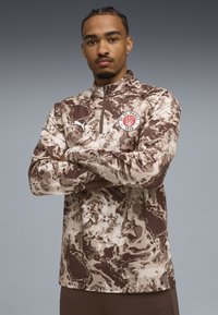 Brun og beige pullover med en kvart lynlås, der har et camouflage-mønster, et logo-patch på brystet og et struktureret stof.