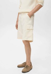 Shorts cargo beiges en coton, dotés de poches latérales, d'une coupe ample, d'une longueur au genou et d'une texture lisse. Associés à des chaussures marron.