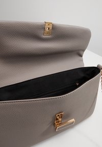 Šedá kožená kabelka se zlatými prvky, s texturovaným povrchem, magnetickým uzávěrem a černým interiérem s kapsou na zip.