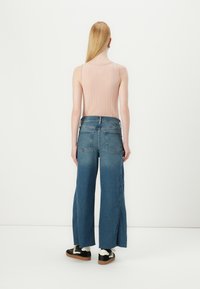 Light pink ribbed tank top, paired with wide-leg blue denim jeans featuring back pockets. The outfit is completed with black and white sneakers.
