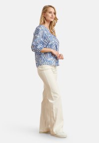 Blauw-witte blouse met patroon en driekwartmouwen, v-hals, gecombineerd met crèmekleurige flared pants en witte sneakers.