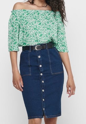 Femme portant un haut fleuri vert à épaules dénudées rentré dans une jupe crayon en jean bleu foncé boutonnée avec une ceinture noire.