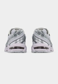 Ζευγάρι ασημένια και λευκά αθλητικά παπούτσια τρεξίματος, εμφανιζόμενα από πίσω, με διακοσμητικό δίχτυ και μαλακές φτέρνες.