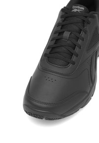 Pantofii sport negri, din piele netedă, cu un design cu șireturi, perforații subtile și o talpă din cauciuc texturat. Logo-ul Reebok este vizibil.