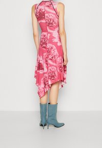 Różowa sukienka z kwiatowym wzorem, bez rękawów, asymetryczny dół, zestawiona z jasnoniebieskimi botkami na obcasie. Gładka tekstura materiału.