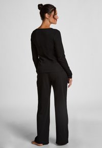 Zwarte longsleeve top en bijpassende broek van zachte stof. De top heeft een vierkante halslijn en de broek heeft een losse pasvorm.