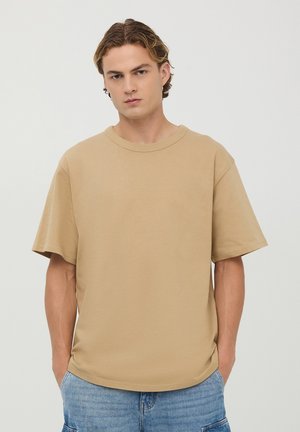 T-shirt in cotone beige con vestibilità rilassata, scollatura rotonda e maniche corte. Texture liscia, design minimale, senza motivi visibili.