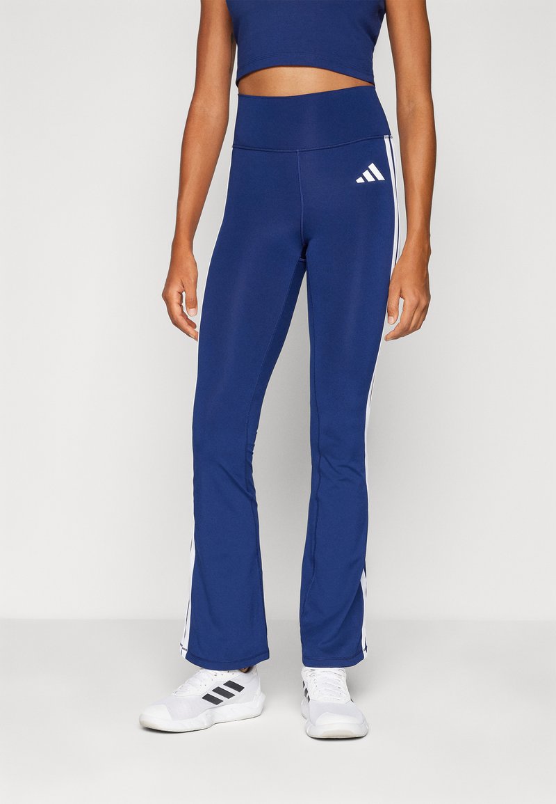Pantalons de sport évasés bleu marine avec des rayures blanches sur les côtés et une taille élastique. Assortis avec des chaussures de sport blanches. Tissu lisse et extensible.