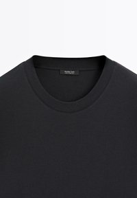 Svart t-shirt med rund halsringning tillverkad av mjuk bomull. Har en slät textur och en etikett synlig på insidan av krageområdet.