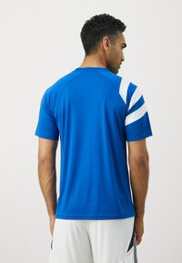 Blå idretts T-skjorte med hvite diagonale striper på skuldrene, korte ermer og en glatt tekstur. Standard passform, minimalistisk design.