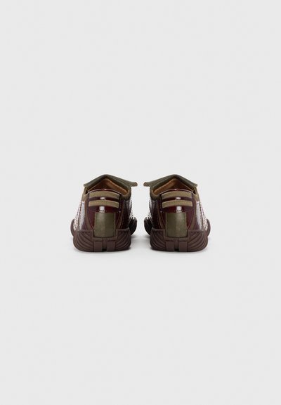 Brown and gold athletic shoes with textured fabric, a reinforced heel, and striped detailing. Features pull tabs for easy wear.