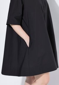Abito nero a maniche corte con vestibilità ampia, tasche laterali e un'apertura sul colletto, realizzato in tessuto morbido e leggero.