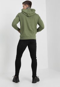 Haut à capuche vert olive avec cordon de serrage, design ajusté, poignets et ourlet côtelés ; associé à un jean skinny noir et des baskets noires.