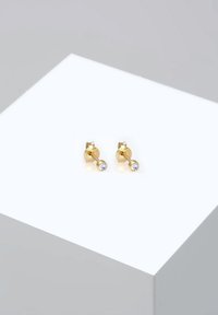 Guldbelagda studs med en rund klar kristallakcent, med en slank och minimalistisk design. Polerad metallyta med en jämn textur.