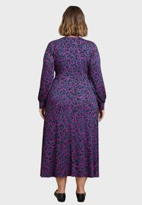 Pitkähihainen mekko, jossa on violetti ja musta leopardikuosis, valmistettu pehmeästä kankaasta, joka ulottuu puoliväliin pohjetta.