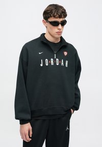 Μαύρο φούτερ με ψηλό γιακά, μισό φερμουάρ, λογότυπο JORDAN σε λευκό και πορτοκαλί και το λογότυπο Nike στο μπροστινό μέρος. Μαλακή υφή υφάσματος.