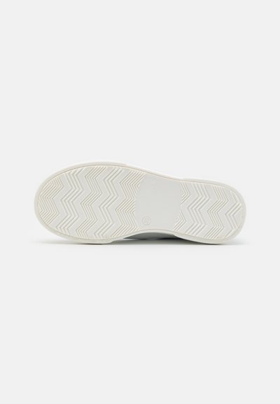 Suela de zapatilla blanca con patrón de tracción en zigzag. Goma texturizada y bordes lisos. Logotipo circular cerca del centro. Talla marcada como 33.