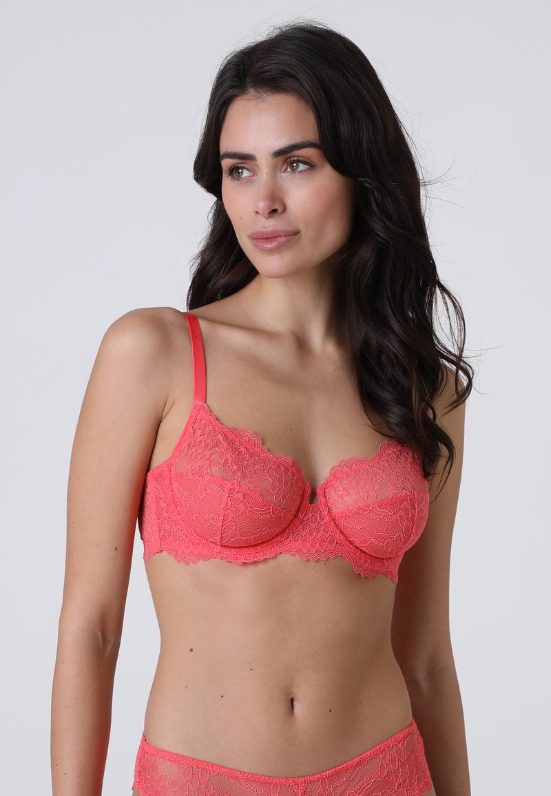 Reggiseno in pizzo corallo con ferretto, motivo floreale, spalline regolabili e bordi scallop. Texture morbida, design semi-trasparente.