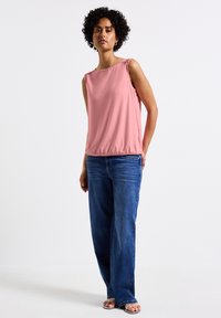 Ärmlös rosa topp med rund halsringning och elastisk fåll, ihop med vida blå jeans. Slät tyg och avslappnad design.