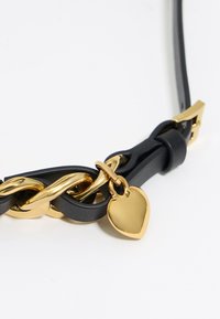 Schwarzes Lederhalsband mit einer goldenen Kette und einem herzförmigen Anhänger aus Gold. Glatte Textur mit einer Mischung aus polierten und matten Oberflächen.