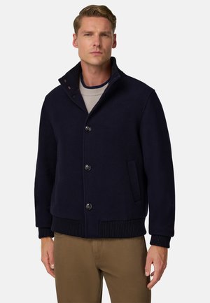 Chaqueta de mezcla de lana azul marino con cuello alto, botones frontales, bolsillos laterales y puños y dobladillo acanalados; diseñada para un ajuste relajado.