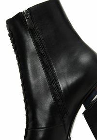 Mustan nahka-ankle boot, jossa on sivuvetoketju, tekstuuripinta ja hienovarainen kudottu yksityiskohta reunan ympäri. Loiva korko, jossa kromiainesta.