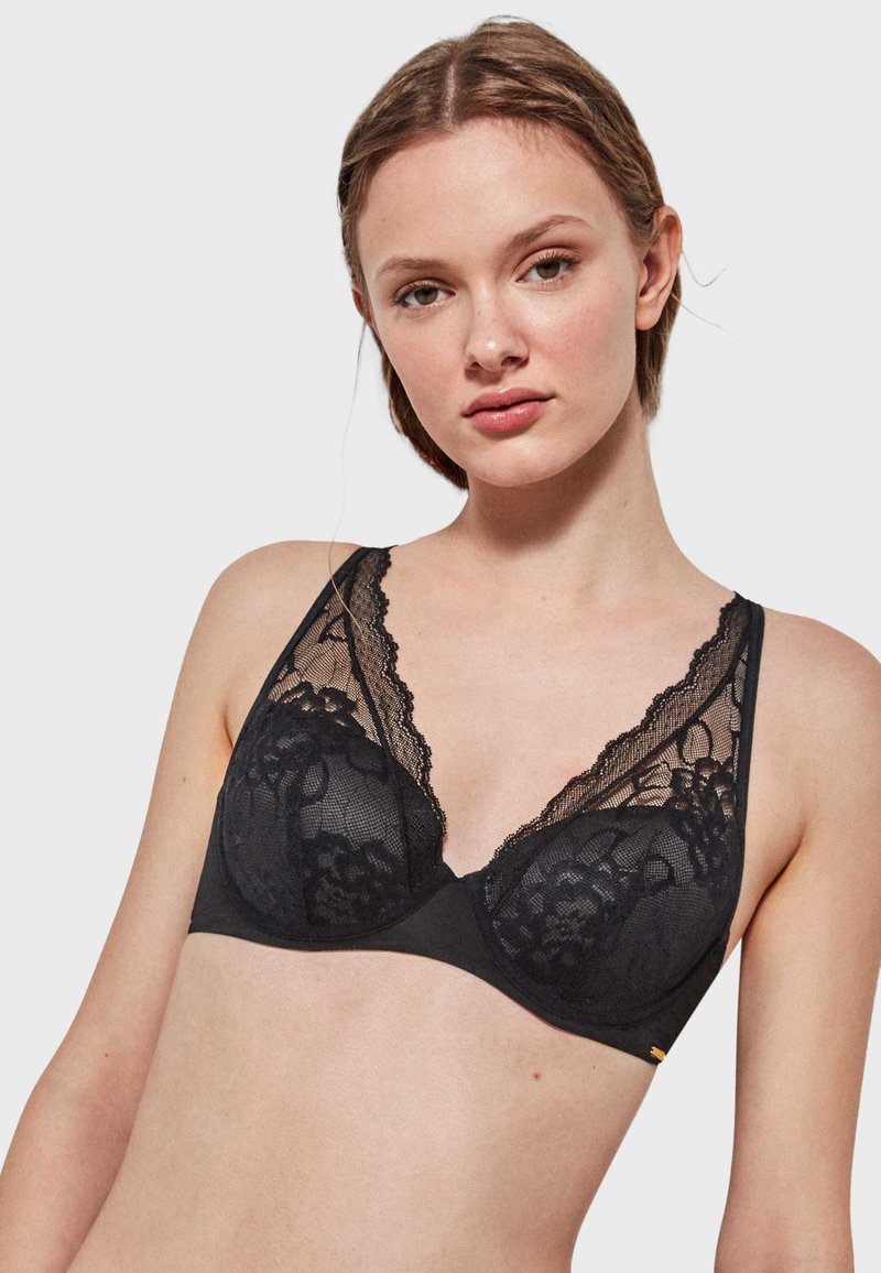 Crna čipkasta bralette sa elegantnim cvjetnim uzorcima, mekim mrežastim prekrivačem, dubokim V-izrezom i podešivim naramenicama. Glatki materijal šalica pruža udobnost.