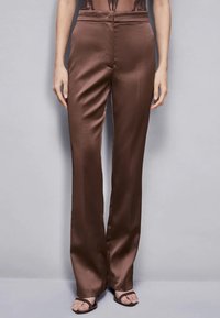Pantaloni in satin marroni con una texture liscia, vita alta e vestibilità sartoriale, dotati di un design a gamba dritta e dettagli delle cuciture minimi.