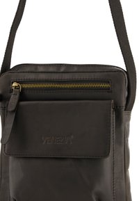 Sort læder crossover-taske med en forlommet lynlås, glat tekstur og præget "VENEZIA" logo. Justerbar stofrem inkluderet.