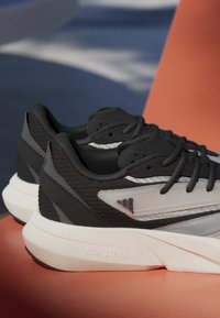 Čierne športové topánky s textúrovaným zvrškom, odrazovými akcentmi a hrubou bielou podrážkou so štítkom "LIGHTSTRIKE." Obsahujú tradičné šnúrky.